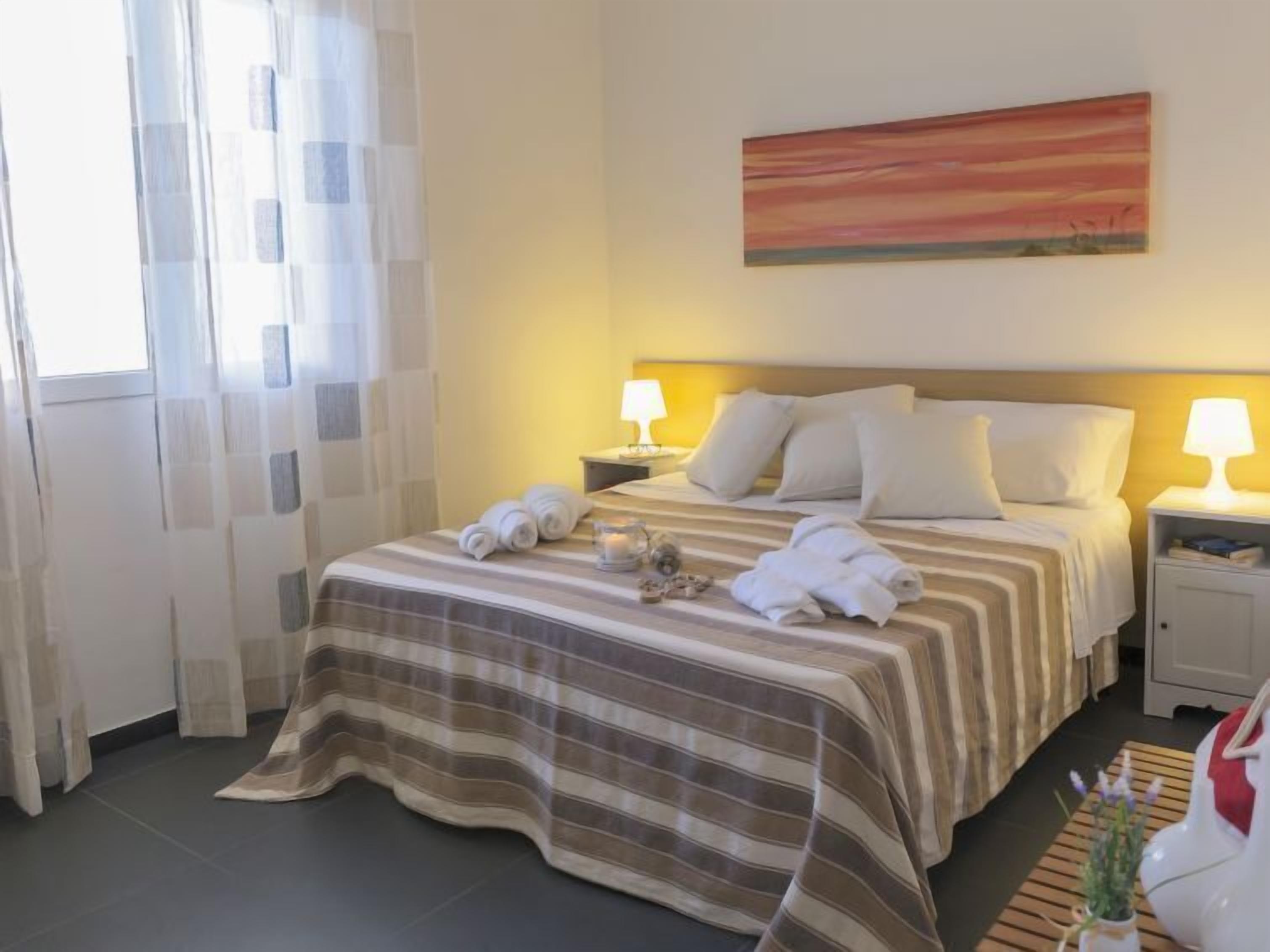 Una camera d'albergo con un letto, due lampade ai comodini, un quadro appeso e una finestra con tende.