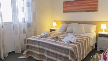 Una camera d'albergo con un letto, due lampade ai comodini, un quadro appeso e una finestra con tende.