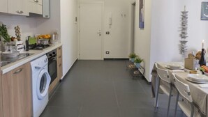 A modern kitchen with a washing machine, a dining area with a table set for two, and a door leading to another room. - Brezza Marina by Interhome (Scicli)
