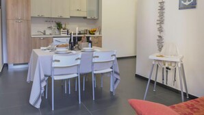 A compact kitchen with white cabinets, a dining table set for four, and a small white chair with a cushion. - Brezza Marina by Interhome (Scicli)