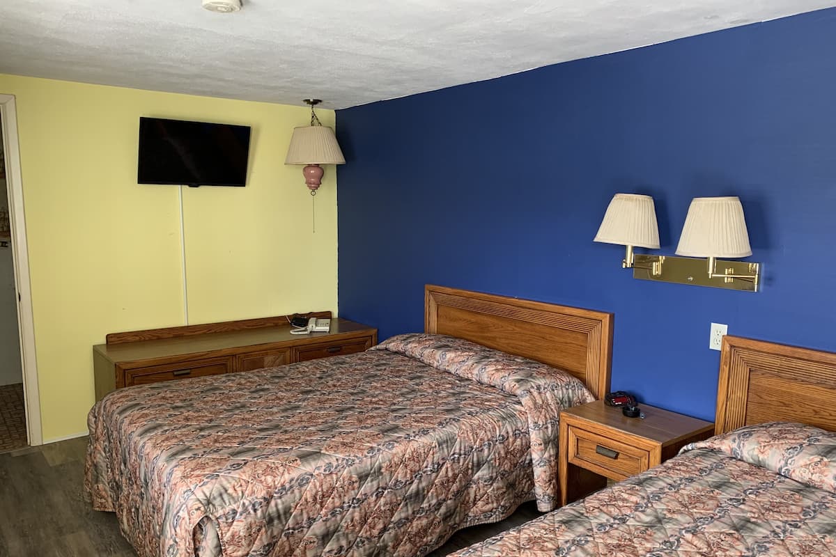 A hotel room with two beds, a TV, bedside lamps, and a wooden nightstand.