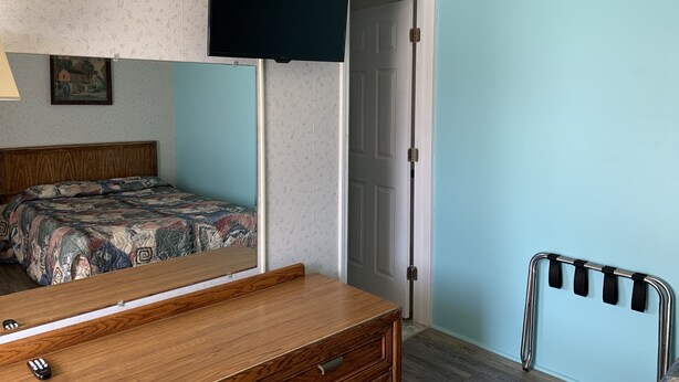 A bedroom with a bed, a dresser, a mirror, a TV, and a door. - Erwin Motel (Painted Post)