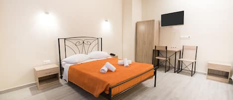 Quarto bem arrumado com cama, mesas de cabeceira, escrivaninha e televisão presa na parede.