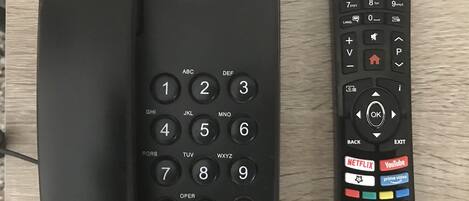 A black telephone and remote control on a wooden surface.
