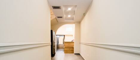 A corridor with a tiled floor, white walls, and a ceiling with recessed lighting.