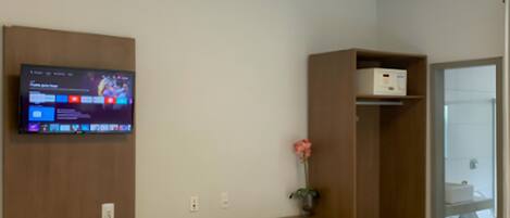 A hotel room with a bed, a desk with a computer, a TV, a small fridge, and a wardrobe.