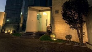 A building with a large glass facade, a brick wall, and a tree in front. - Oasis Hotel (Araguaina)