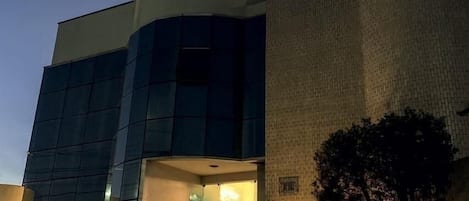 Un edificio con una amplia fachada de vidrio, una pared de ladrillo y un árbol en la parte delantera.