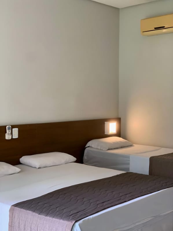 A hotel room with two beds, a wooden headboard, a wall-mounted air conditioner, and bedside lamps.