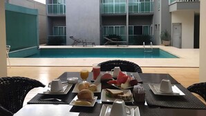 A poolside breakfast setup with a table, chairs, and a view of a modern building with balconies. - Oasis Hotel (Araguaina)