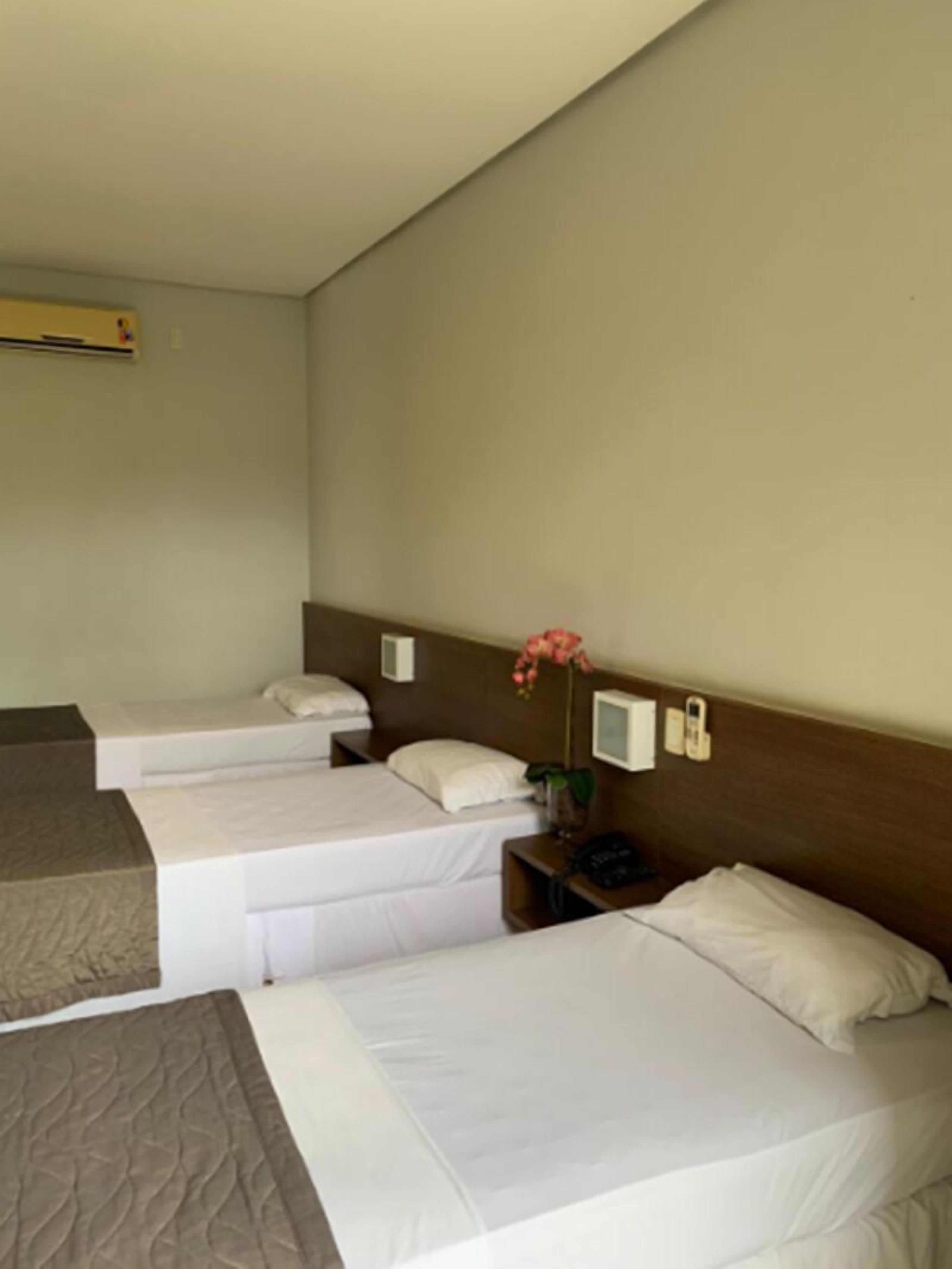 A hotel room with three single beds, a bedside table with a phone, a small TV, and a wall-mounted air conditioner.
