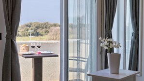 A balcony with a table set for two, a vase with white flowers, and a scenic view of a forested area.