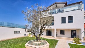 A modern two-story house with a well-maintained lawn, a stone planter with a tree, and a clear sky.