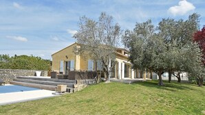 Una casa de dos pisos con piscina, pared de piedra y césped.