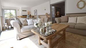 Un salón amplio con un sofá color beige, una mesa de centro de madera con velas y vistas al exterior a través de un ventanal corredero.