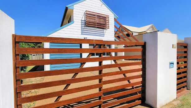 Un bâtiment blanc avec un toit en pente et un portail en bois doté de barreaux horizontaux.