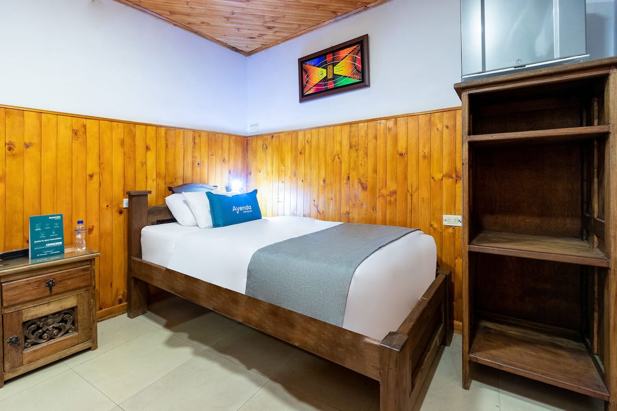 A wooden-paneled room with a bed, a nightstand, a shelf, and a wall-mounted TV.