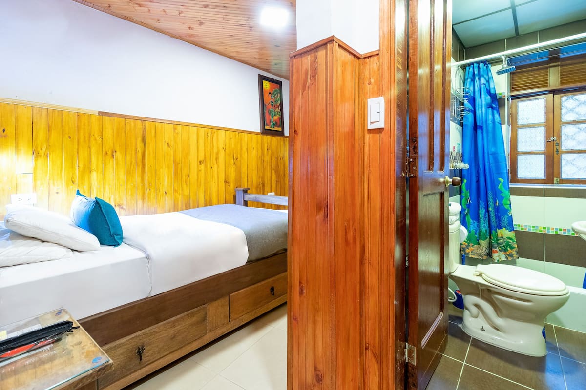 A room with a bed, wooden paneling, a toilet, and a shower curtain.