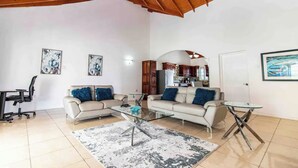 A spacious living area with two sofas, a glass coffee table, a dining table, and a kitchen in the background. - Runaway Bay Gem Villa (Runaway Bay)