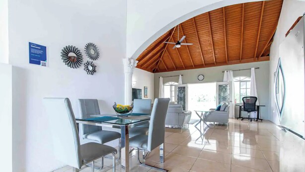 A spacious dining area with a glass table and chairs, a ceiling fan, and decorative wall art. - Runaway Bay Gem Villa (Runaway Bay)