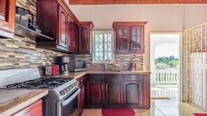 A kitchen with dark wooden cabinets, a gas stove, a microwave, and a window with a view of greenery outside. - Runaway Bay Gem Villa (Runaway Bay)