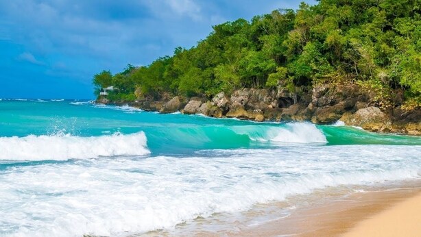 A beach with turquoise waters, a sandy shore, and a rocky cliff with dense greenery. - I Heart JA Me Lo Dio Dios Ocho Rios (Ocho Rios)