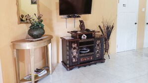A living room with a television, a decorative cabinet, a side table with a vase, and a door with a 'No Smoking' sign. - I Heart JA Me Lo Dio Dios Ocho Rios (Ocho Rios)