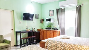 A room with two beds, a desk, a chair, a television, a microwave, and a window with curtains. - I Heart JA Willow Garden Retreat-Mona (Kingston)