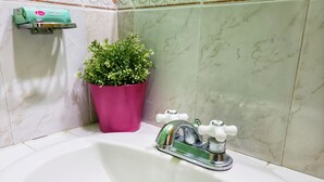 A bathroom with a white sink, a green faucet, a pink plant, and a soap dispenser on the wall. - I Heart JA Willow Garden Retreat-Mona (Kingston)