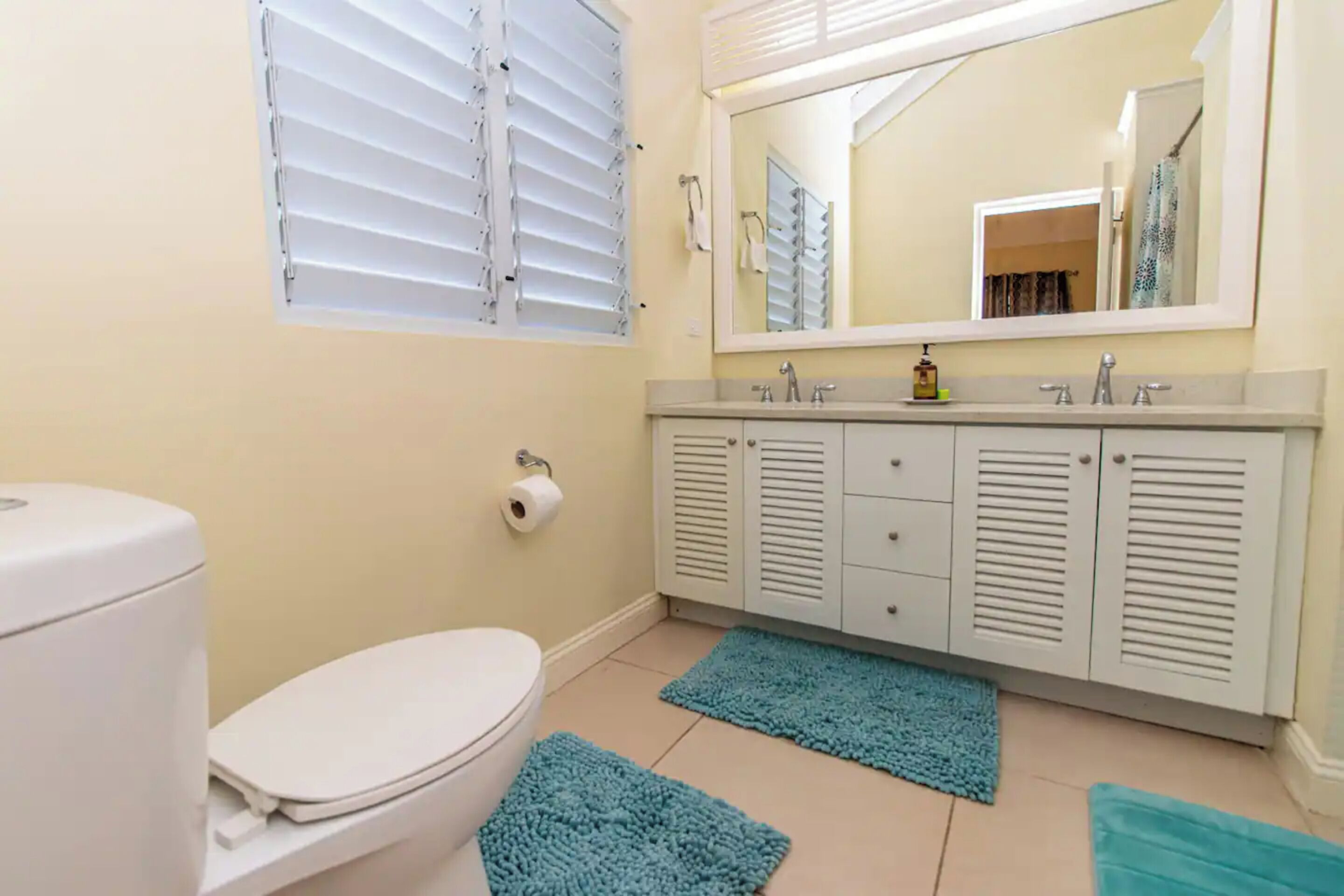 Een badkamer met een toilet, een wastafel met spiegel erboven en een kast met lades.