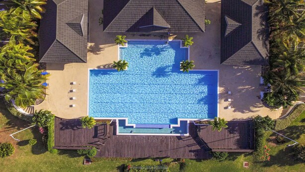 An aerial view of a resort with a central swimming pool surrounded by palm trees and lounge chairs. - I Heart JA  Coastal DreamVIlla-Richmond Estates (St. Ann's Bay)