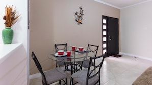 A dining area with a glass table, four chairs, and red cups. - I Heart JA Affordable Luxury at The Bromptons (Kingston)