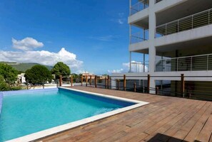 Une piscine sur le toit, dotée d’une terrasse en bois et entourée d’un immeuble moderne avec des balcons.