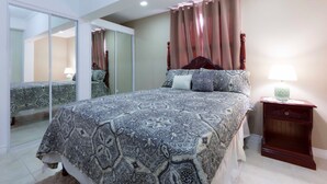 A bedroom with a large bed, a mirror, and a nightstand with a lamp. - I Heart JA Affordable Luxury at The Bromptons (Kingston)
