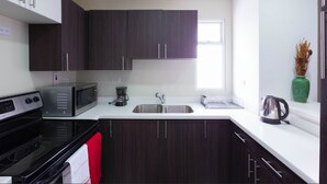 A modern kitchen with dark cabinets, a microwave, a coffee maker, and a kettle. - I Heart JA Affordable Luxury at The Bromptons (Kingston)