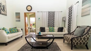 A living room with a sofa, armchair, and coffee table. There is a clock on the wall and a window with curtains. - Serenity Retreat Villa Drax Hall (Ocho Rios)