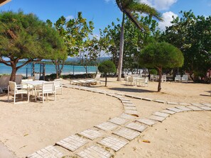 A beachside seating area with tables and chairs, surrounded by trees and a view of the sea. - I Heart JA Serdos (Tower Isle)