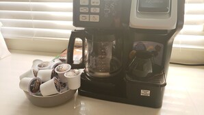 A coffee maker with a digital display, a coffee pot, and a coffee cup holder with disposable cups. - I Heart JA Fairway (Kingston)
