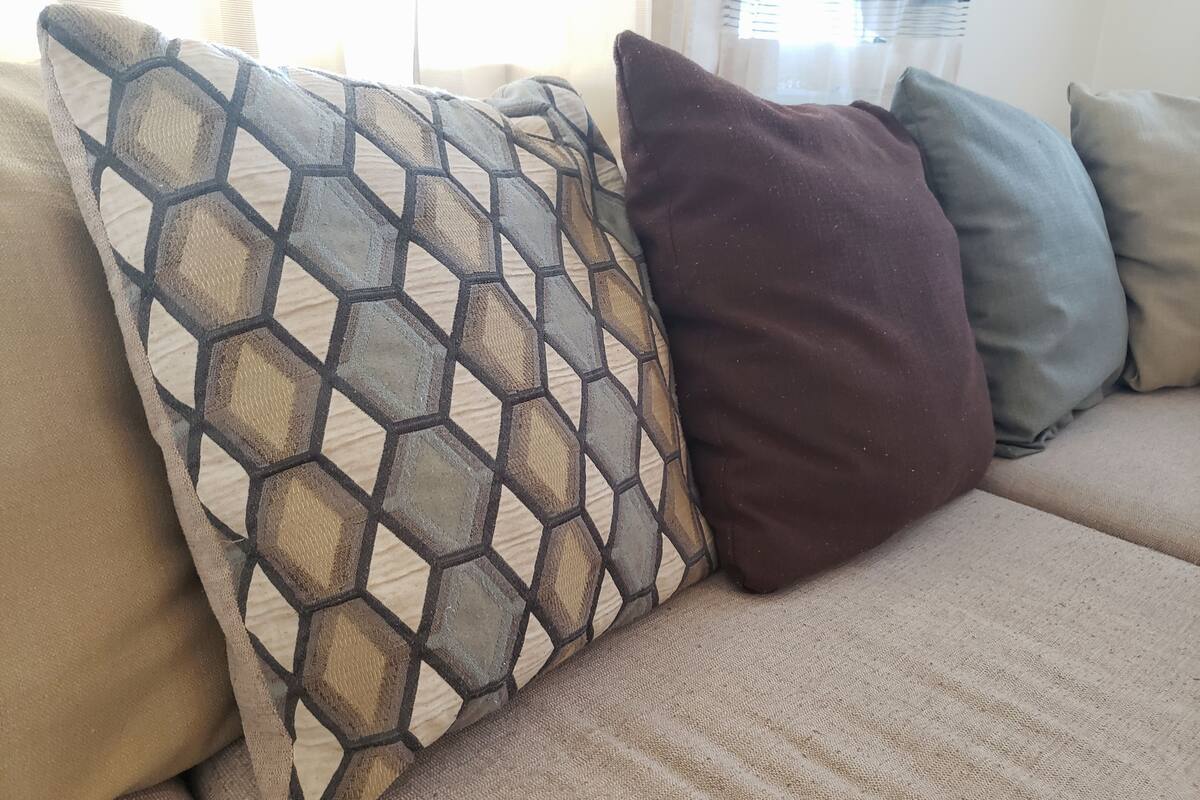 A beige sofa with three cushions: one with a geometric pattern, one solid brown, and one solid gray.