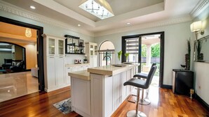 A spacious kitchen with a central island, white cabinetry, and a bar area with stools.