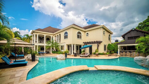 A large house with a swimming pool, lounge chairs, and a pergola.