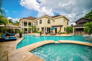 Una casa grande con piscina, sillones de descanso y una pérgola.