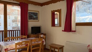 A cozy room with a wooden dining table, chairs, a sofa, a TV, and a window with curtains. - Wifi, 300m from ski slopes, 3rd floor, swimming pool, balcony, parking, tv, ski locker, 35m² (Puy-Saint-Vincent)