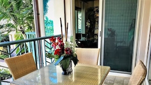 A glass-top table with wicker chairs, a vase with flowers, and a view of the outdoors. - Family Oasis at Waipouli! Our Getaway Incudes: Beach, Pool Resort and Fun! (Kapaʻa)