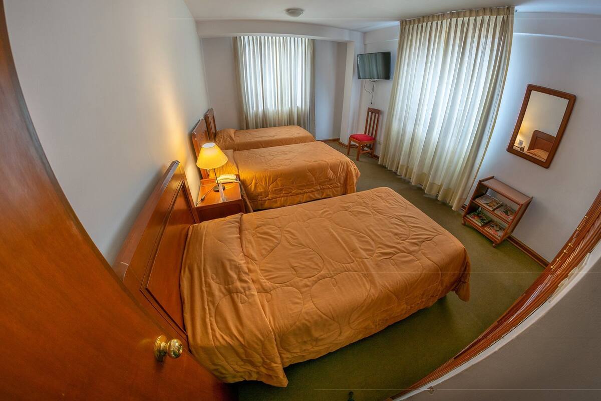 A hotel room with two beds, a TV, a desk with a lamp, and a small bookshelf.