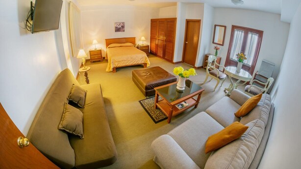 A well-lit, modern hotel room with a sofa, a bed, a dining table, and a TV mounted on the wall. - Hotel Incasol (Jesús Nazareno)