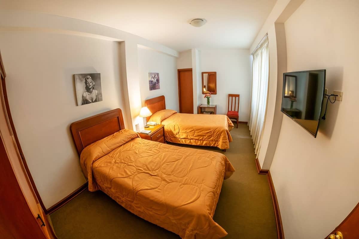 A hotel room with two beds, a TV, a mirror, and artwork on the walls.