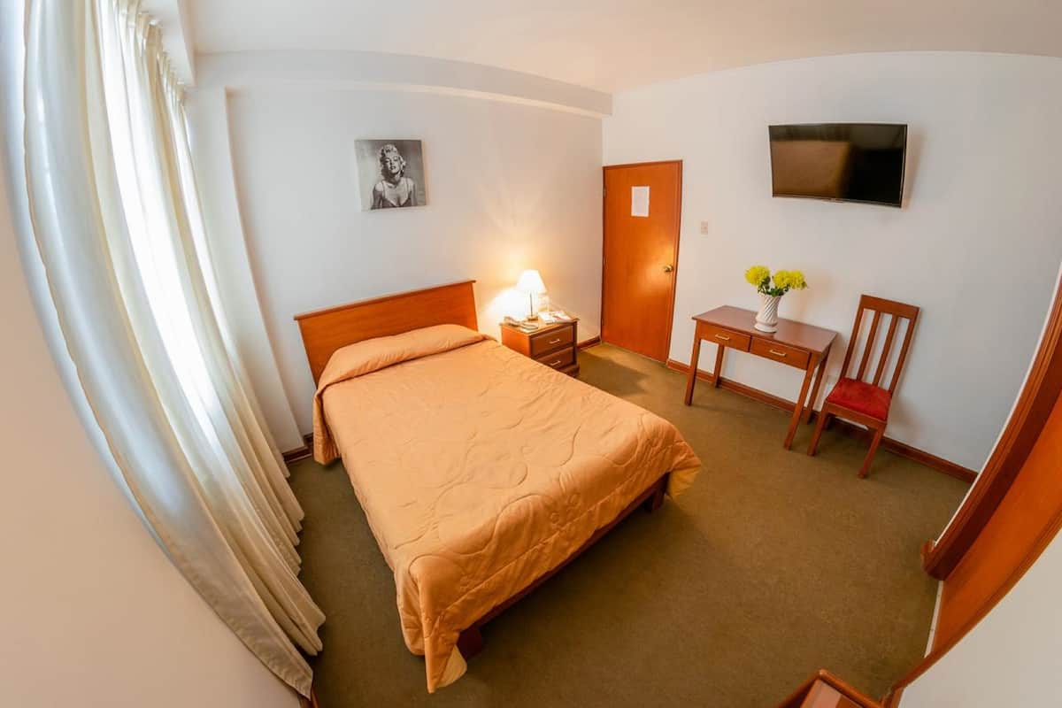 A hotel room with a bed, a desk with a chair, a TV, and a door.