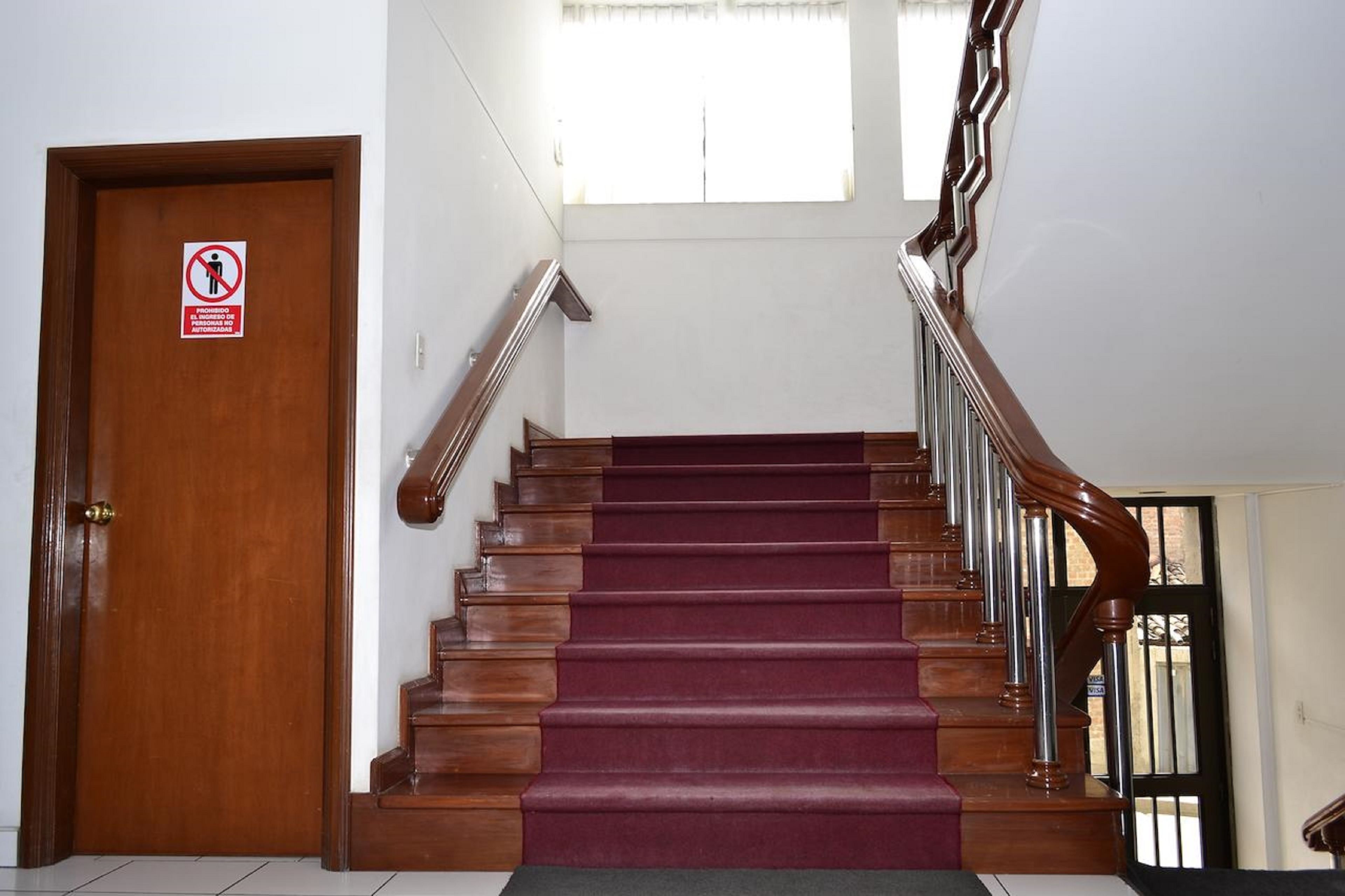A wooden staircase with a red carpet, a door with a no entry sign, and a window above.
