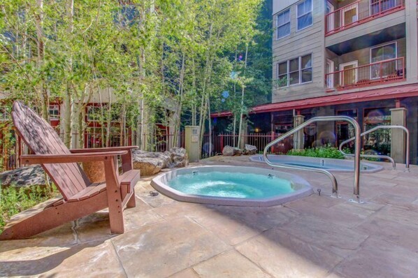 Un área de piscina con un jacuzzi, una silla de descanso de madera y un patio de piedra.